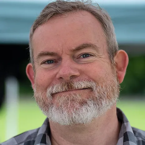 A man with a gray beard and checkered shirt, perhaps fresh from a session at Davenport Pelvic Therapy, smiles warmly at the camera.